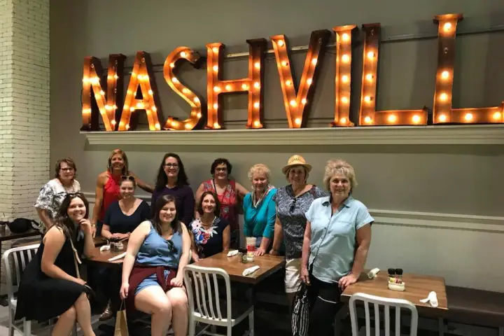 A group of women smiling under a lit sign reading 
