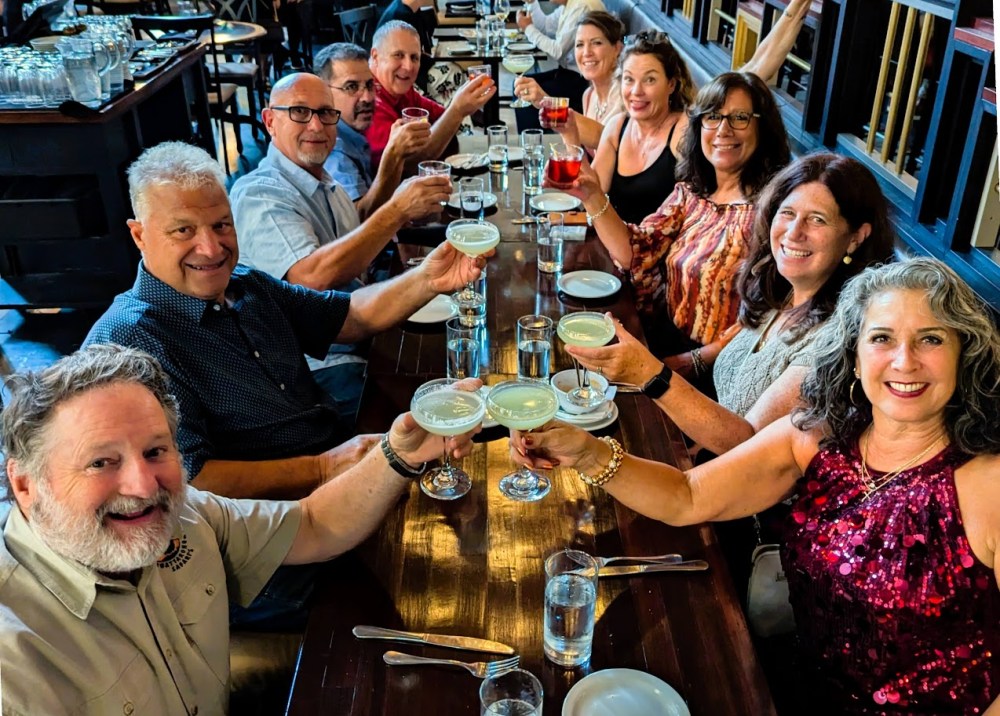 Group of people at a long table in a restaurant, raising glasses and smiling.